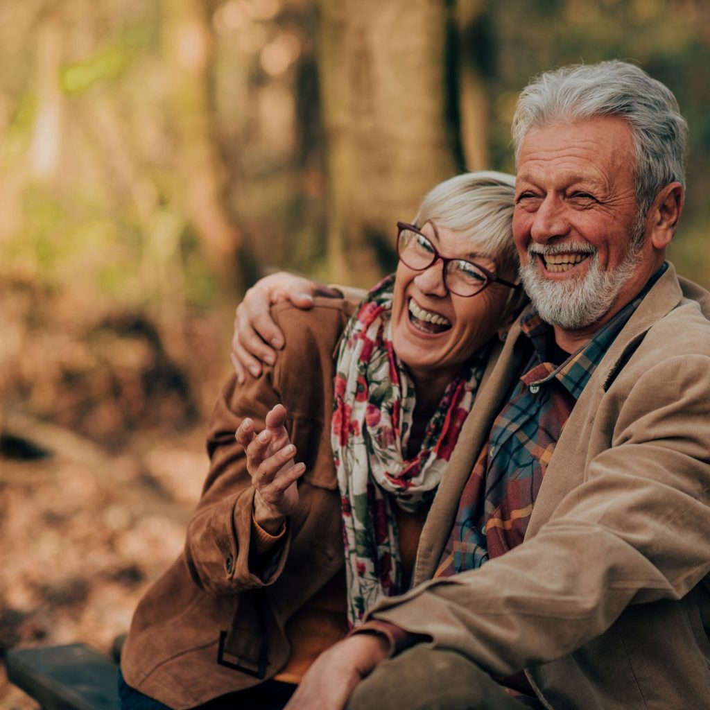 Old couple hugging each other on a bench in an autumnal forest.