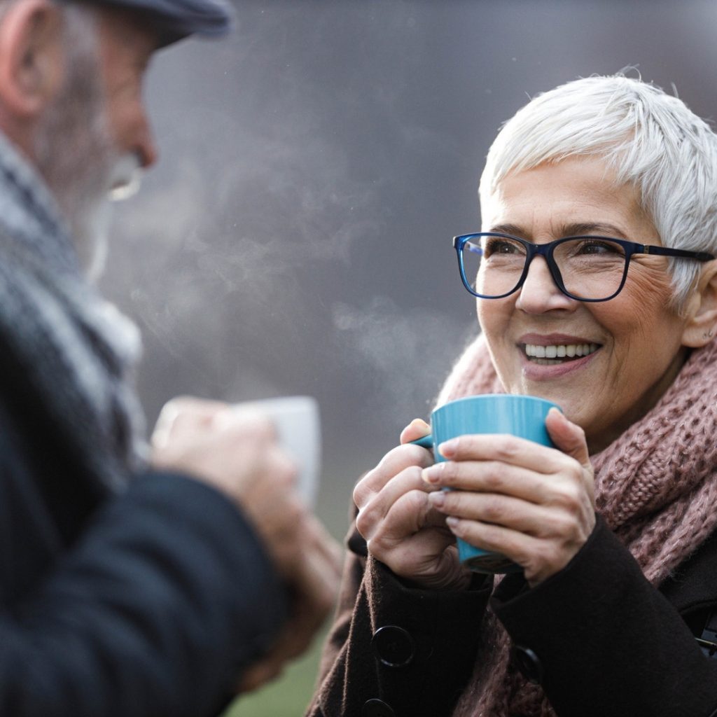Elderley couple enjoying a hot drink outside in the cold as they warm into winter.