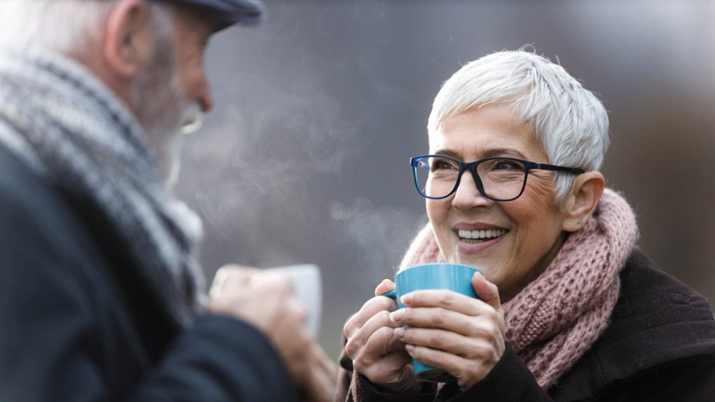 Elderley couple enjoying a hot drink outside in the cold as they warm into winter.