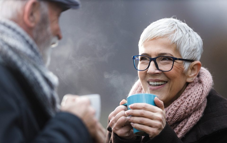 Elderley couple enjoying a hot drink outside in the cold as they warm into winter.